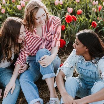 Three girls sitting near flowers, laughing